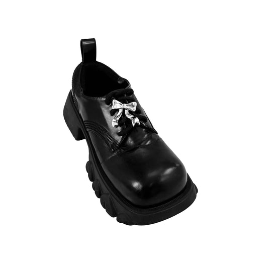 Silver bow-shaped shoe accessory clipped onto the laces of a black sneaker or boot.