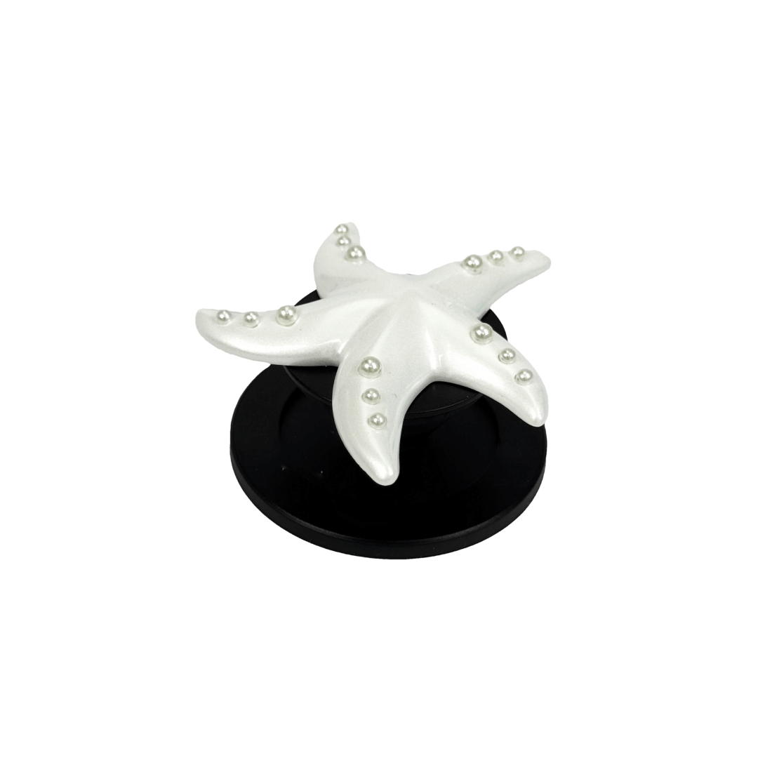 Glossy white, silver, gold and pink starfish-shaped phone grip with embedded rhinestones, mounted on a black base and attached to a gray iPhone case.