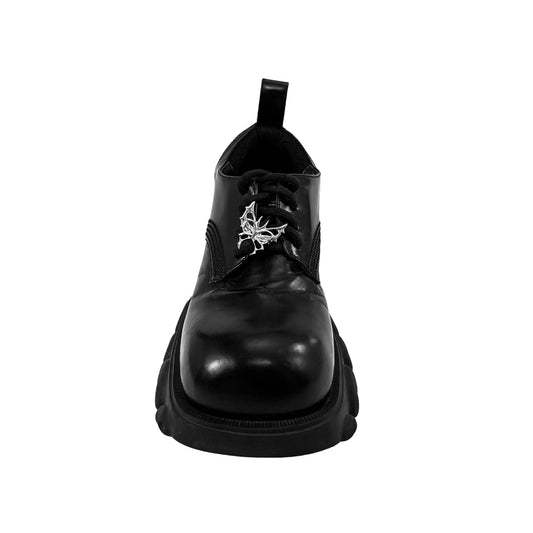 Sculptural chrome wing-shaped shoe accessory clipped onto the side or lace area of a black leather shoe.