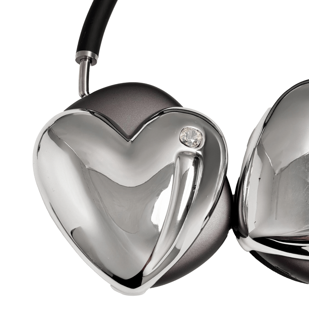 Metallic heart-shaped AirPods Max cover in silver, pink, red and black, with a smooth 3D sculpted surface and a single crystal stud detail.