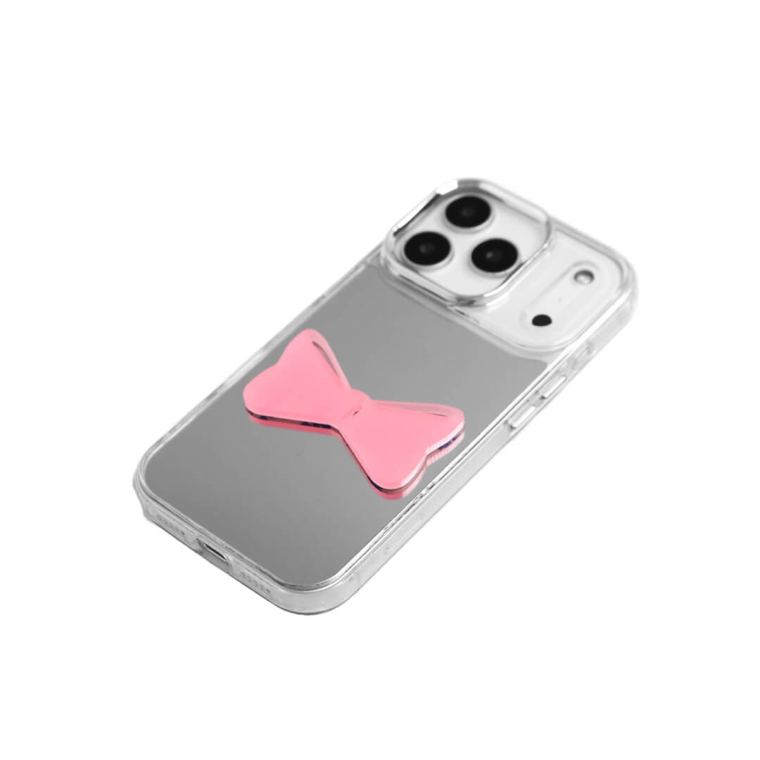 A modern iPhone case featuring a 3D acrylic bow/ribbon ornament. Available in Sakura Pink and Azure Blue acrylic finishes. The case is shown on both a Reflective Silver metallic base and a Clear Transparent base, showcasing a minimalist yet playful fashion aesthetic.