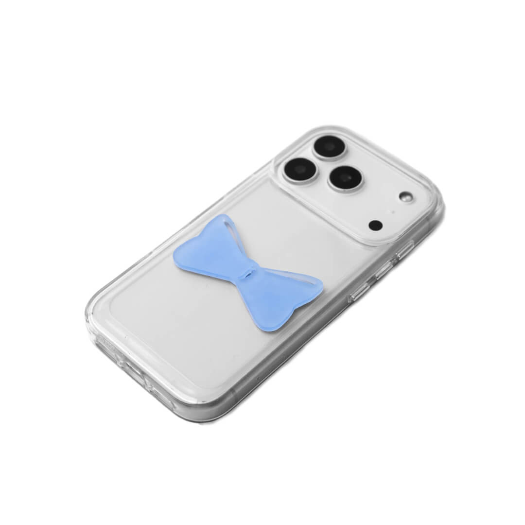A modern iPhone case featuring a 3D acrylic bow/ribbon ornament. Available in Sakura Pink and Azure Blue acrylic finishes. The case is shown on both a Reflective Silver metallic base and a Clear Transparent base, showcasing a minimalist yet playful fashion aesthetic.
