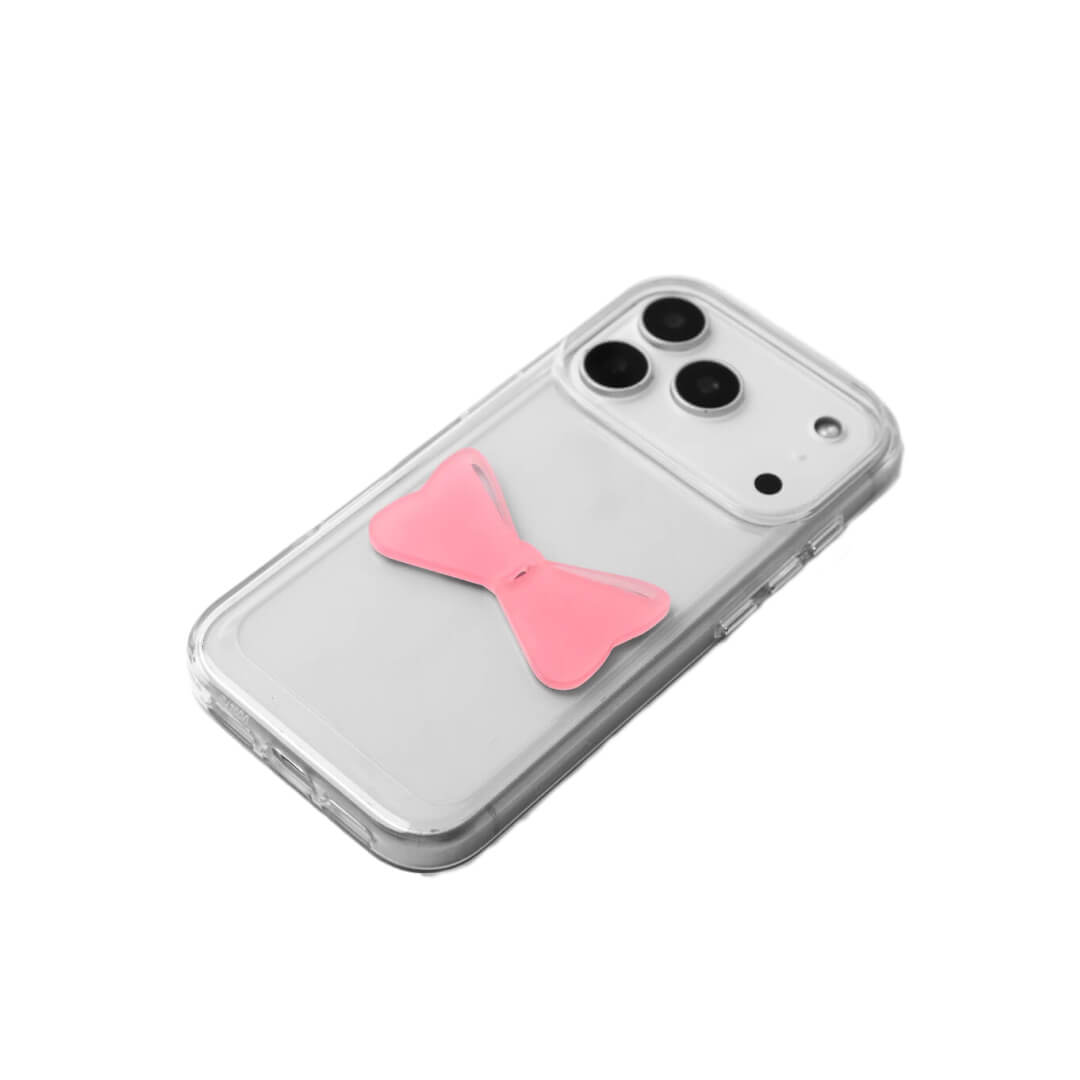 A modern iPhone case featuring a 3D acrylic bow/ribbon ornament. Available in Sakura Pink and Azure Blue acrylic finishes. The case is shown on both a Reflective Silver metallic base and a Clear Transparent base, showcasing a minimalist yet playful fashion aesthetic.