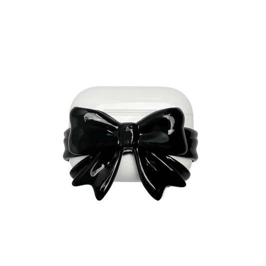 A pair of protective covers for Apple AirPods (or AirPods Pro) charging case. Each cover is white and features a large, 3D sculpted bow charm centered on the front. One bow is glossy black and the other is pure white.