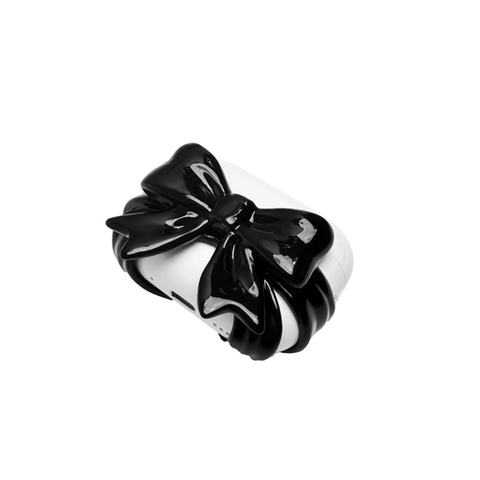 A pair of protective covers for Apple AirPods (or AirPods Pro) charging case. Each cover is white and features a large, 3D sculpted bow charm centered on the front. One bow is glossy black and the other is pure white.