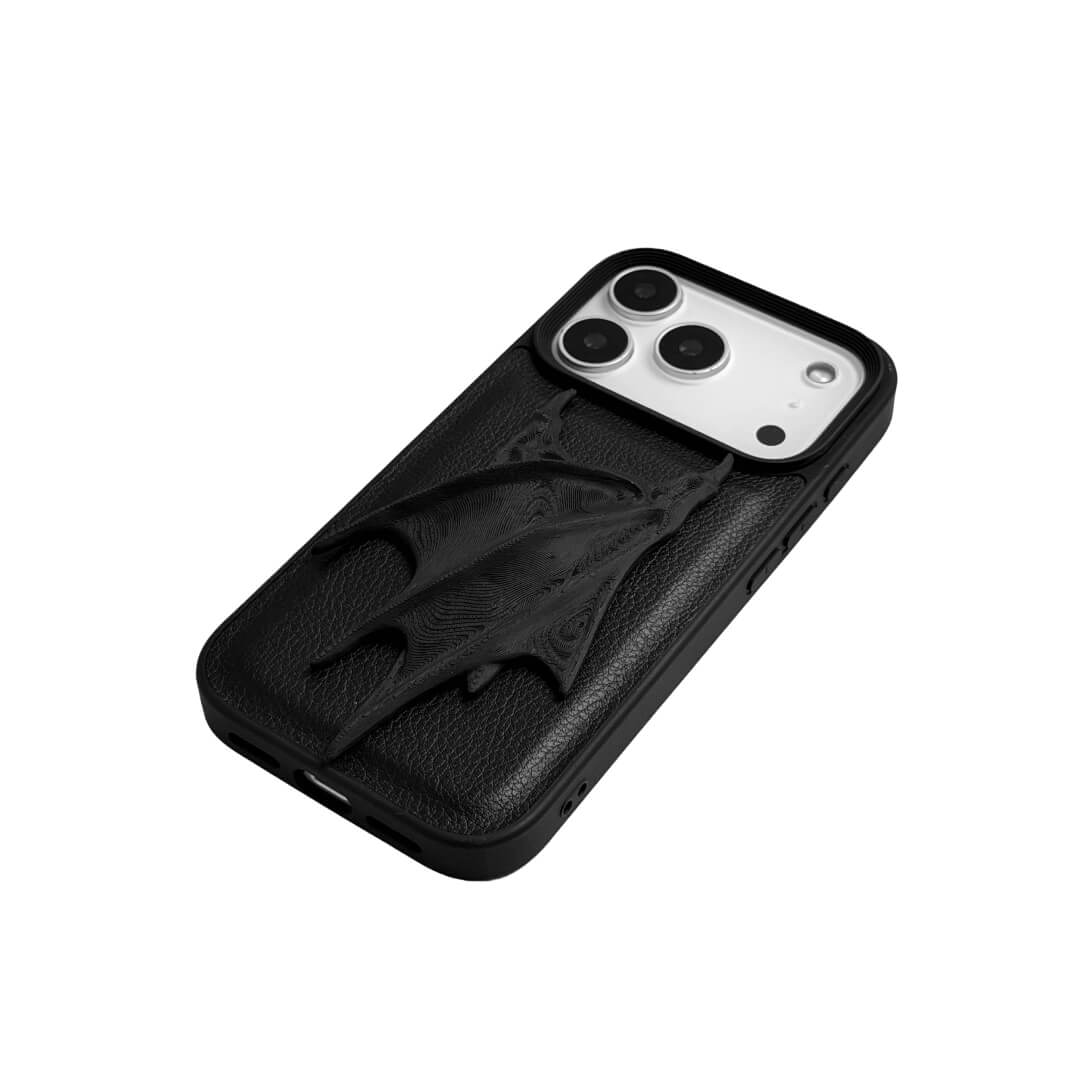 A high-concept iPhone case featuring a large, 3D-printed double demon wing ornament with a natural matte black finish. The wings are shown in two variations: one mounted on a Clear Transparent base, and another on a premium Black Litchi Leather textured base, highlighting the intricate, organic details of the sculptural wings.