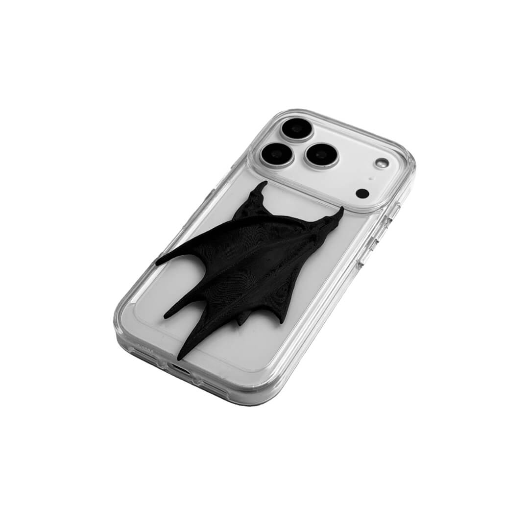 A high-concept iPhone case featuring a large, 3D-printed double demon wing ornament with a natural matte black finish. The wings are shown in two variations: one mounted on a Clear Transparent base, and another on a premium Black Litchi Leather textured base, highlighting the intricate, organic details of the sculptural wings.