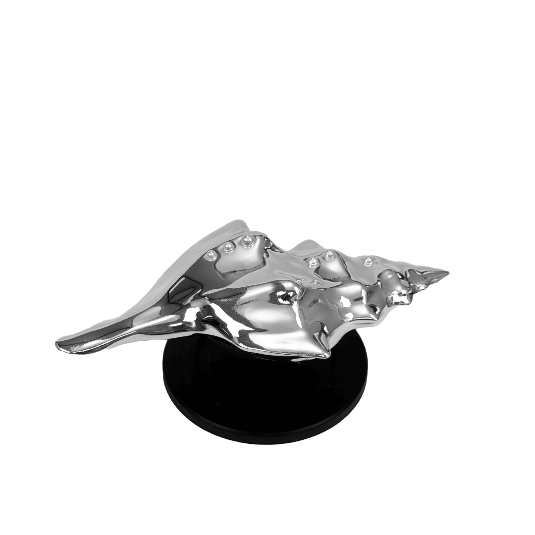 Glossy silver, white and yellow conch shell-shaped phone grip with sculptural ridges and rhinestone accents, mounted on a black base and attached to a gray iPhone case.