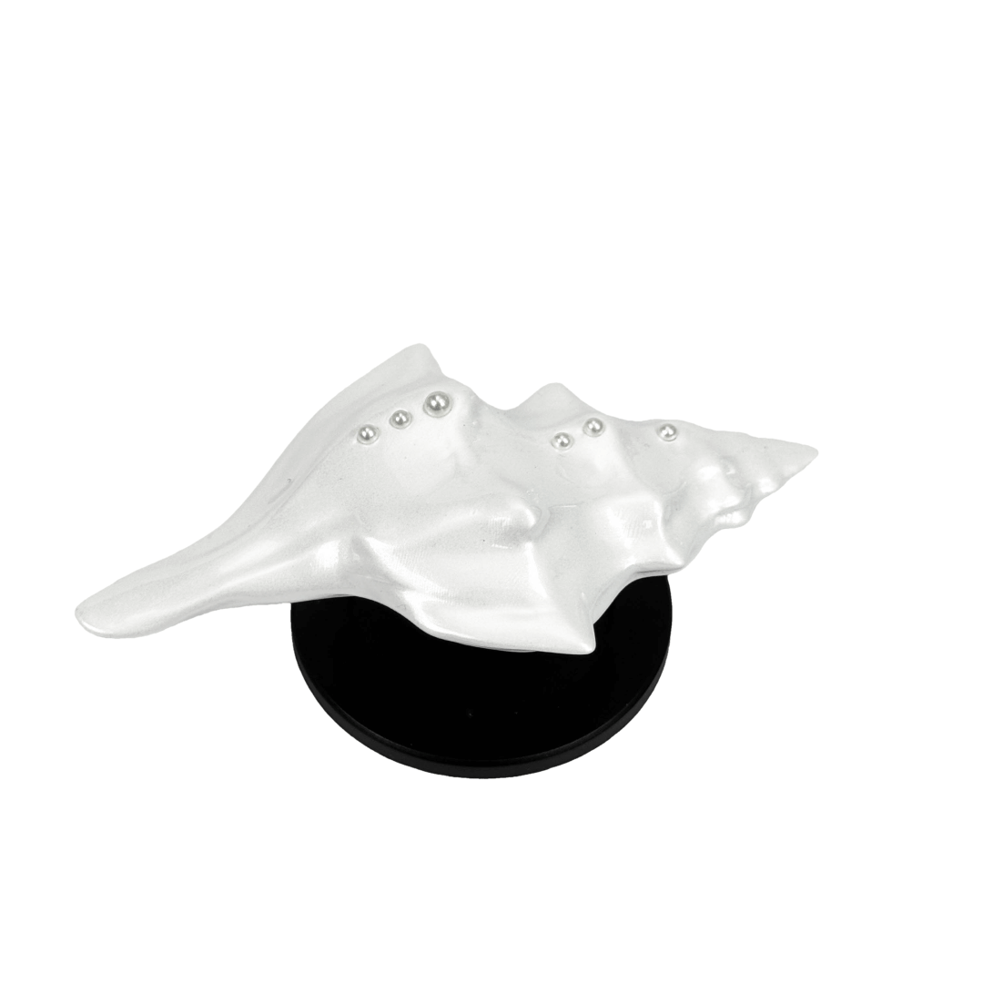 Glossy silver, white and yellow conch shell-shaped phone grip with sculptural ridges and rhinestone accents, mounted on a black base and attached to a gray iPhone case.