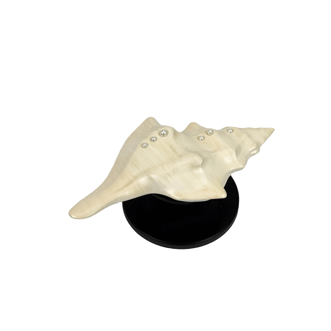 Glossy silver, white and yellow conch shell-shaped phone grip with sculptural ridges and rhinestone accents, mounted on a black base and attached to a gray iPhone case.