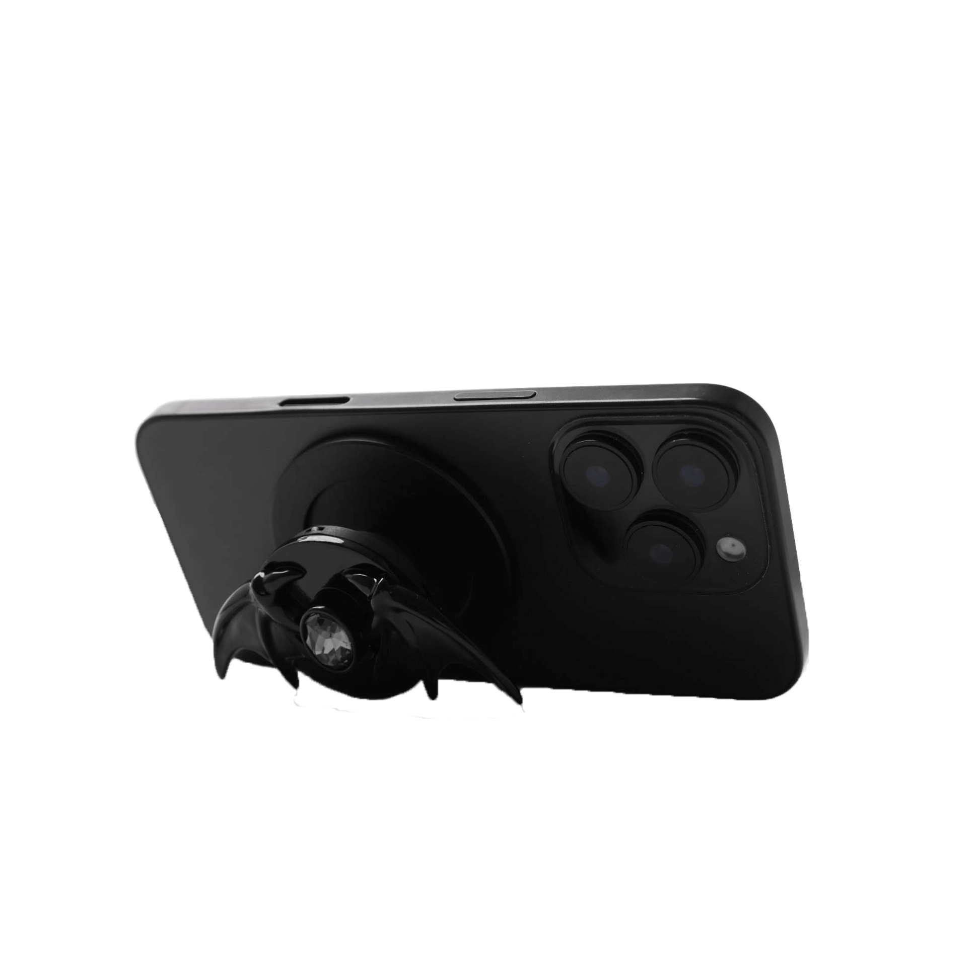 A 3D sculpted demon wing phone grip featuring a central black Swarovski crystal. The product is shown in two finish options: a reflective Silver Chrome that contrasts with the dark gem, and a Sleek Black finish for a full monochromatic look. It is designed to function as both a secure hand grip and a desktop stand.