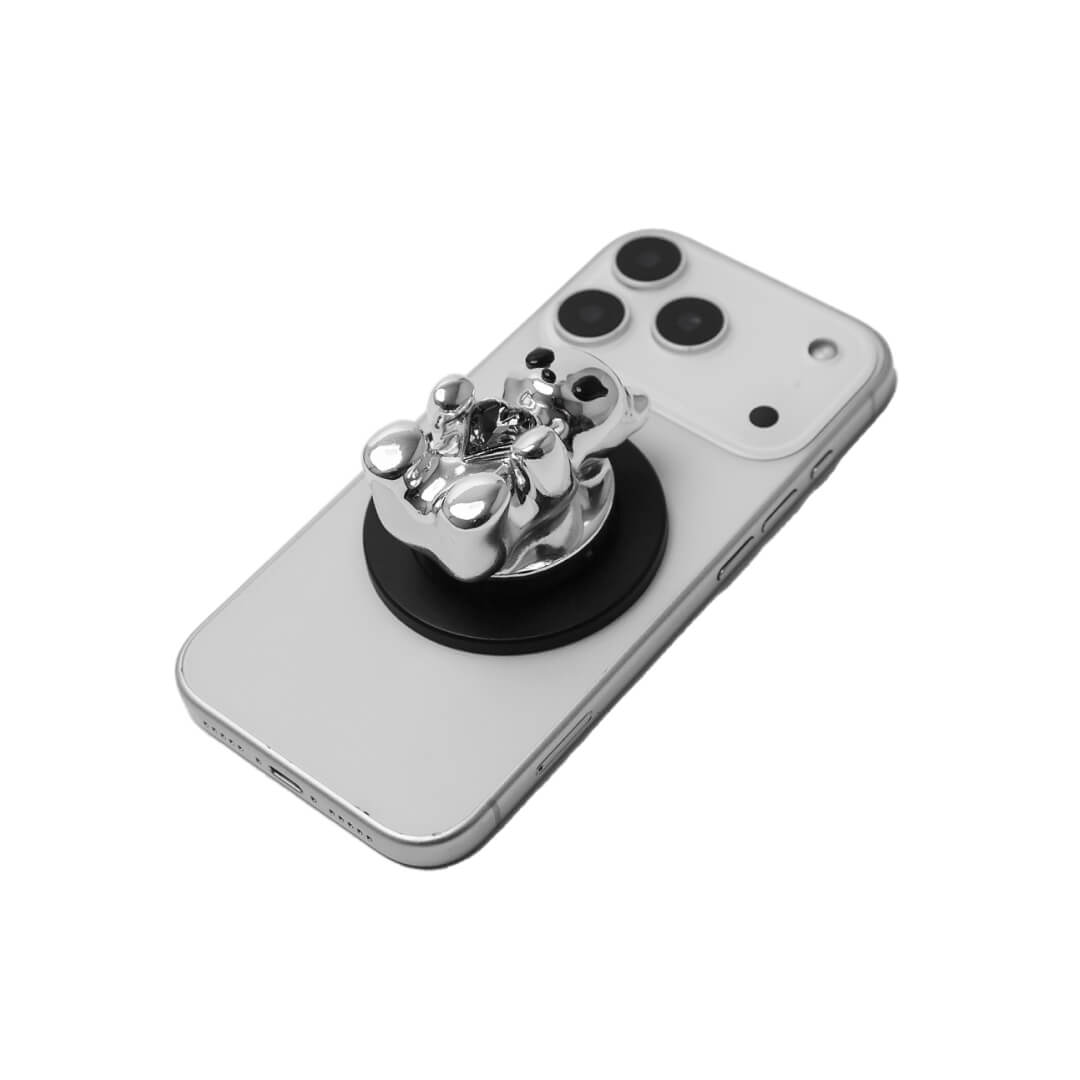 The Gem Gummy Bear phone grip collection featuring the sculpted 3D bear holding a sparkling central heart gem, shown in both the reflective Silver Chrome and glossy Black finish options.