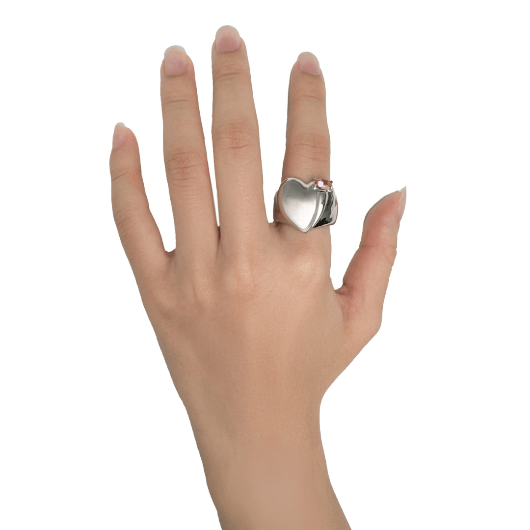 Wide band ring with a heart-shaped design and a pink Swarovski crystal centerpiece.