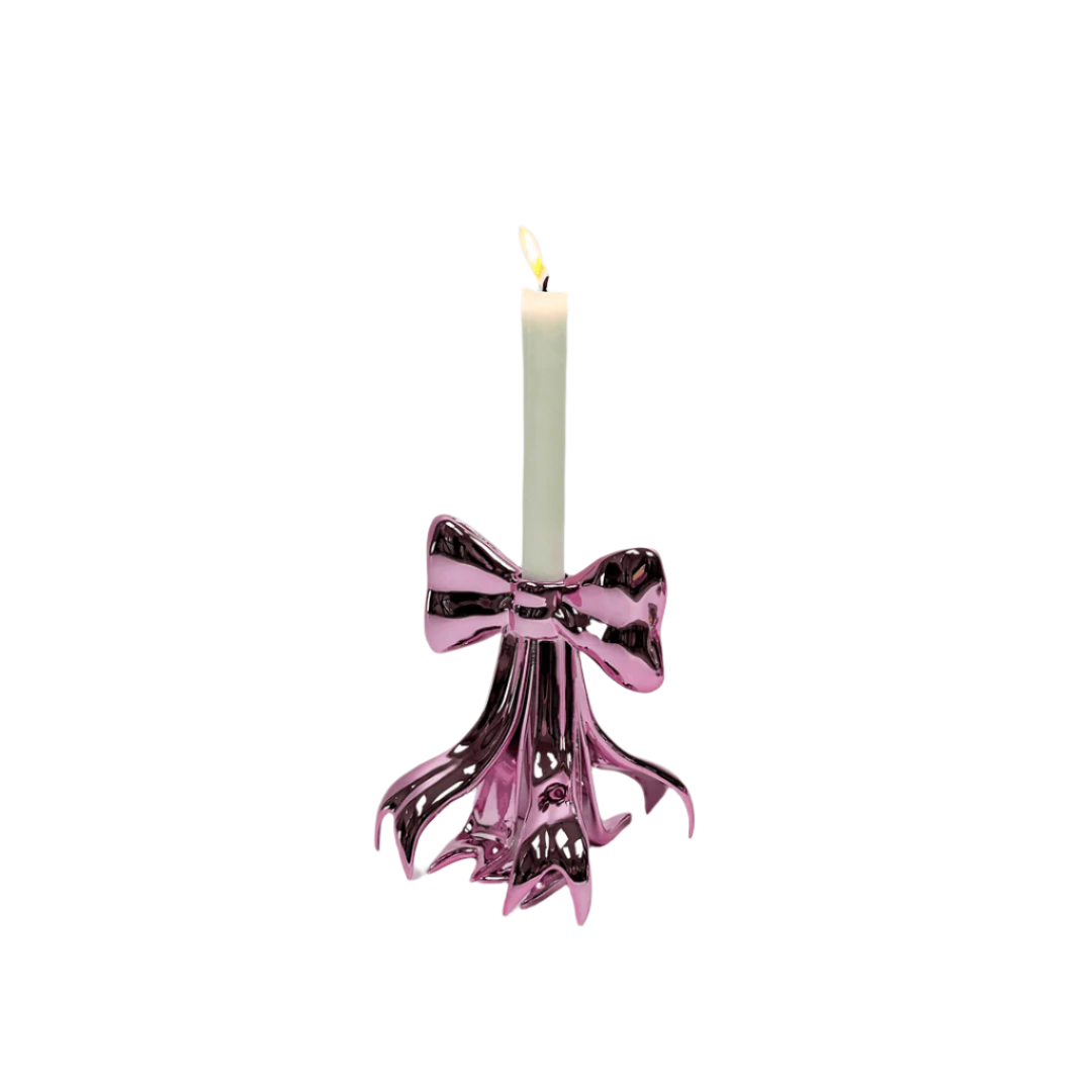 Glossy pink candleholder shaped like a sculptural bow – metallic luster finish with flowing ribbon base supporting a lit taper candle, blending whimsy and elegance