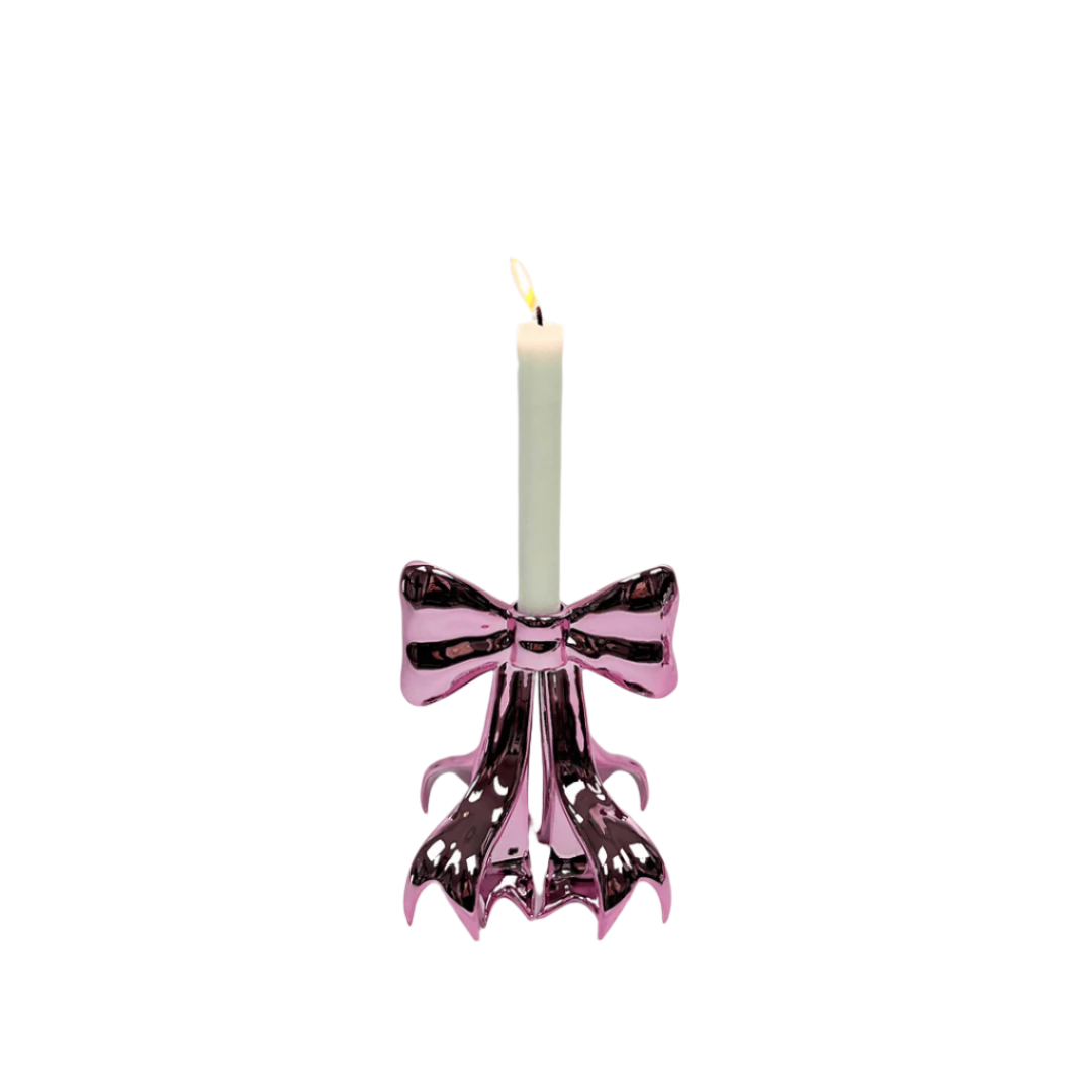 Glossy pink candleholder shaped like a sculptural bow – metallic luster finish with flowing ribbon base supporting a lit taper candle, blending whimsy and elegance