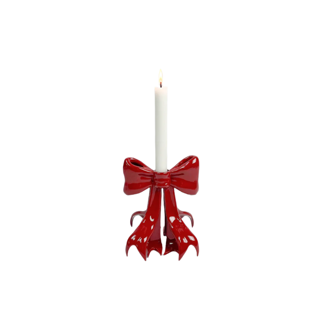 Glossy pink candleholder shaped like a sculptural bow – metallic luster finish with flowing ribbon base supporting a lit taper candle, blending whimsy and elegance