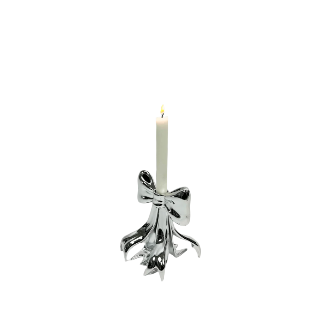 Glossy pink candleholder shaped like a sculptural bow – metallic luster finish with flowing ribbon base supporting a lit taper candle, blending whimsy and elegance