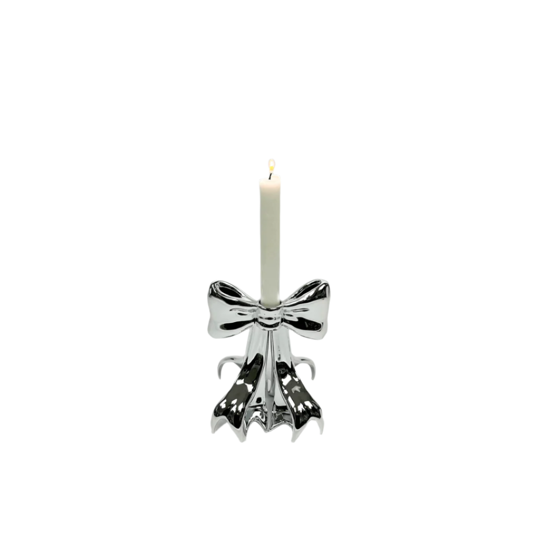 Glossy pink candleholder shaped like a sculptural bow – metallic luster finish with flowing ribbon base supporting a lit taper candle, blending whimsy and elegance