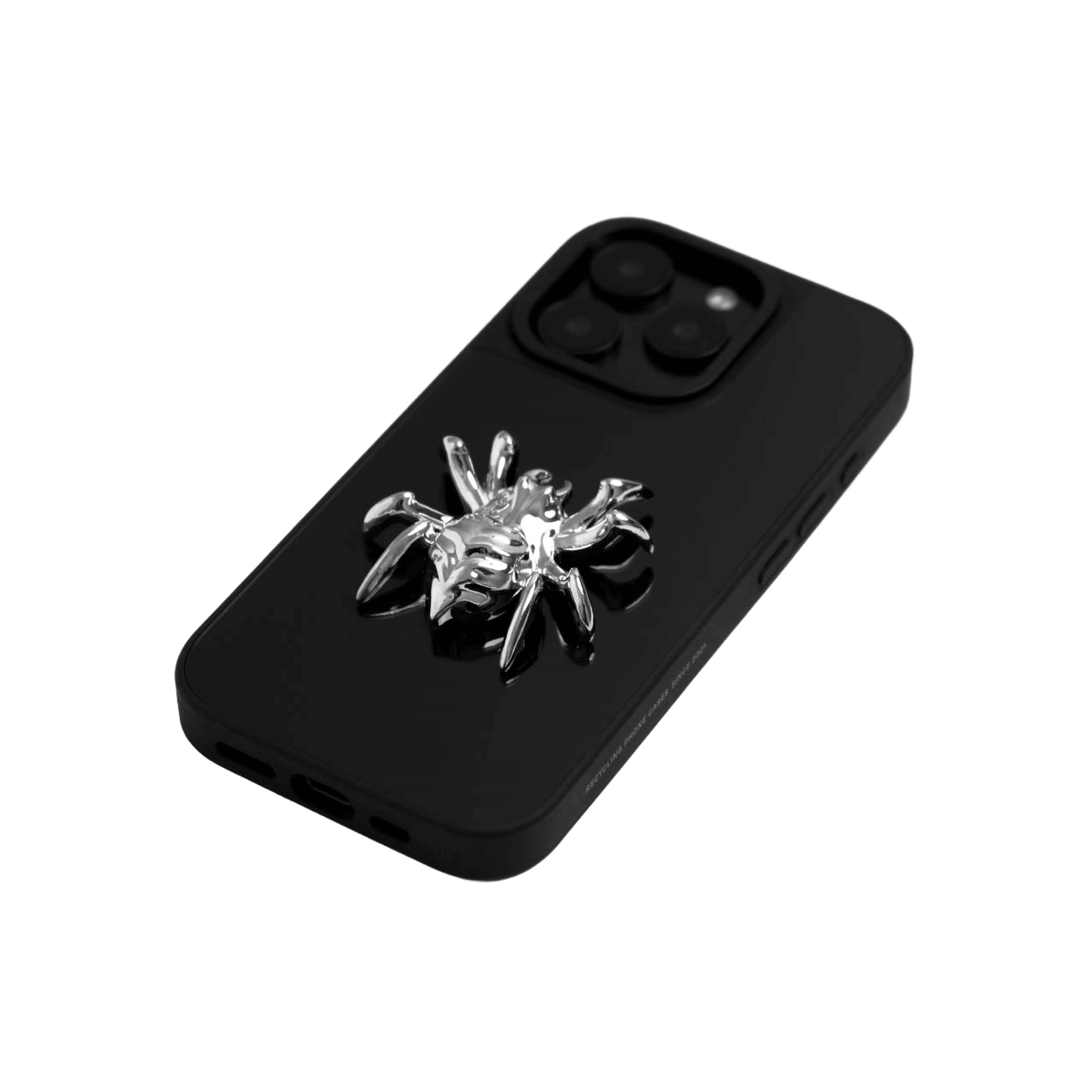 A collection of four black iPhone cases, each adorned with a distinct silver 3D metal emblem: a prominent bow tie, a sleek circular stud, an intricate spider, and a stylized four-point cross.