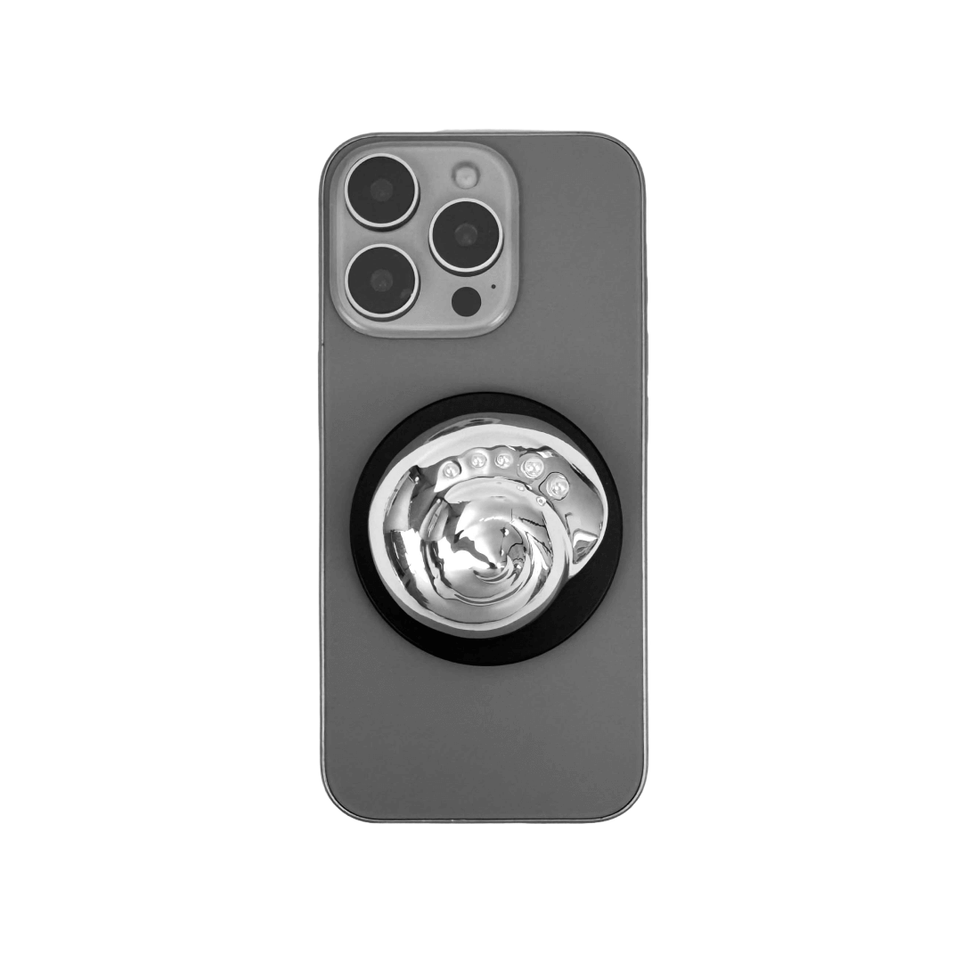 Glossy silver, white spiral shell phone grip with rhinestone accents – mounted on a matte black base and attached to a gray iPhone case