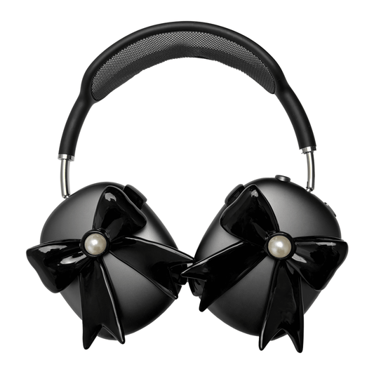 A pair of protective covers for the AirPods Max headphones, featuring a large, 3D bow charm on each ear cup cover. One set is matte black with black bows, and the other is metallic silver with white bows. A white pearl is centered on each bow.
