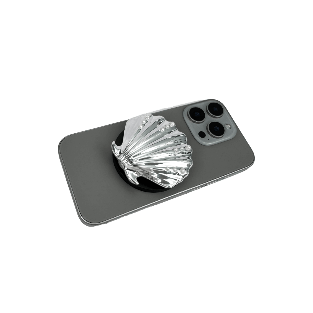 Gradient silver, white and yellow-to-pink scallop shell phone grip with rhinestone accents, mounted on a black base and attached to a gray iPhone case