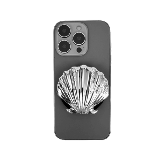 Gradient silver, white and yellow-to-pink scallop shell phone grip with rhinestone accents, mounted on a black base and attached to a gray iPhone case