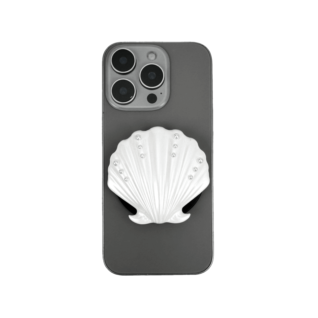 Gradient silver, white and yellow-to-pink scallop shell phone grip with rhinestone accents, mounted on a black base and attached to a gray iPhone case
