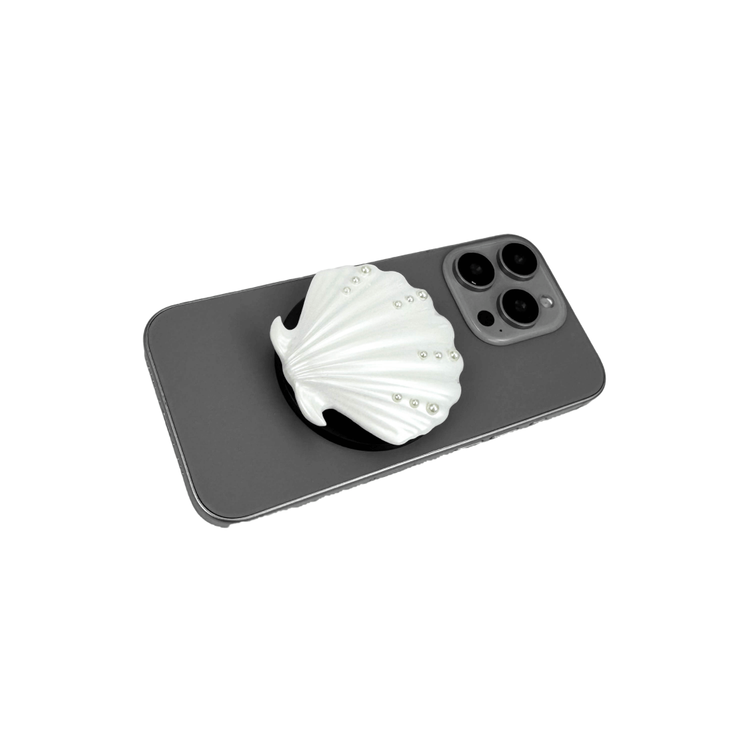Gradient silver, white and yellow-to-pink scallop shell phone grip with rhinestone accents, mounted on a black base and attached to a gray iPhone case