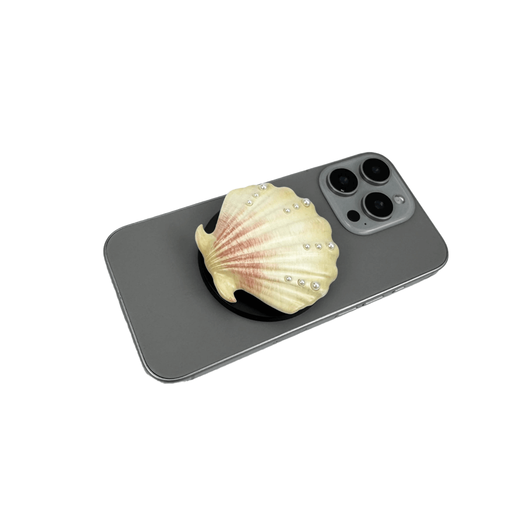 Gradient silver, white and yellow-to-pink scallop shell phone grip with rhinestone accents, mounted on a black base and attached to a gray iPhone case