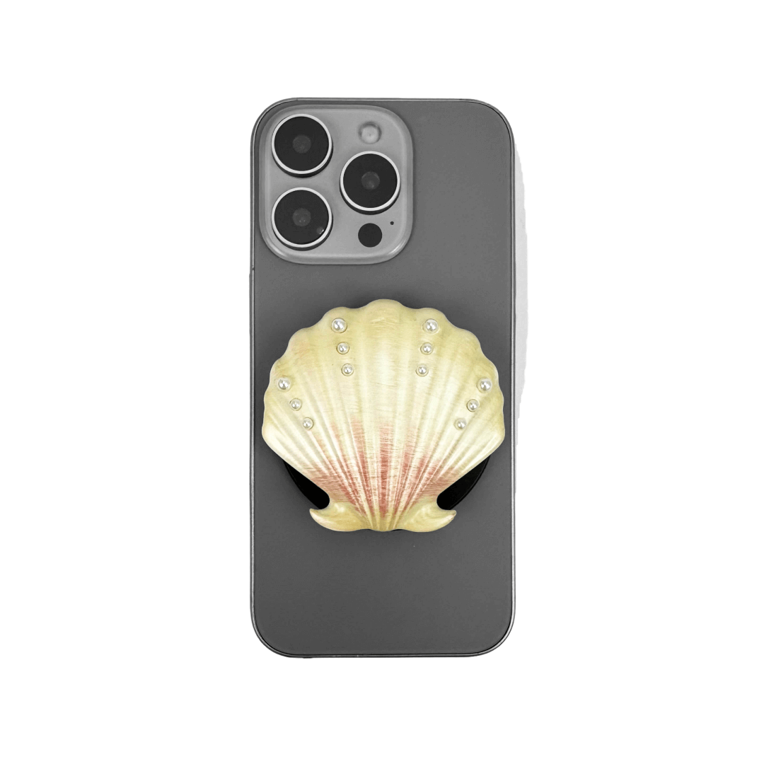 Gradient silver, white and yellow-to-pink scallop shell phone grip with rhinestone accents, mounted on a black base and attached to a gray iPhone case