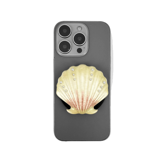 Gradient silver, white and yellow-to-pink scallop shell phone grip with rhinestone accents, mounted on a black base and attached to a gray iPhone case