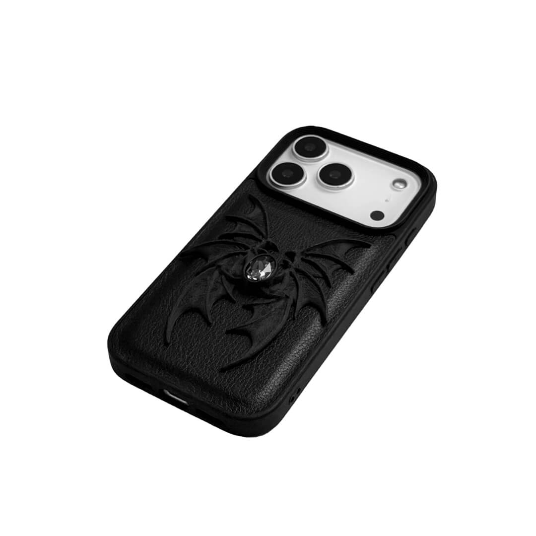 A high-concept iPhone case featuring a 3D-printed quad-wing demon design in a natural matte black finish, centered with a sparkling black Swarovski crystal. The design is shown on a Clear Transparent base and a Black Litchi Leather textured base, highlighting the intricate, layered skeletal wing structure and the dark gemstone detail.