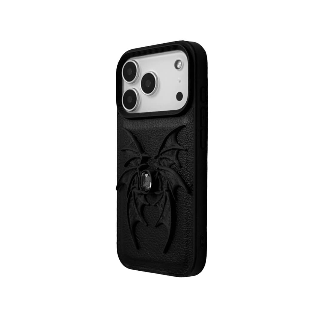 A high-concept iPhone case featuring a 3D-printed quad-wing demon design in a natural matte black finish, centered with a sparkling black Swarovski crystal. The design is shown on a Clear Transparent base and a Black Litchi Leather textured base, highlighting the intricate, layered skeletal wing structure and the dark gemstone detail.