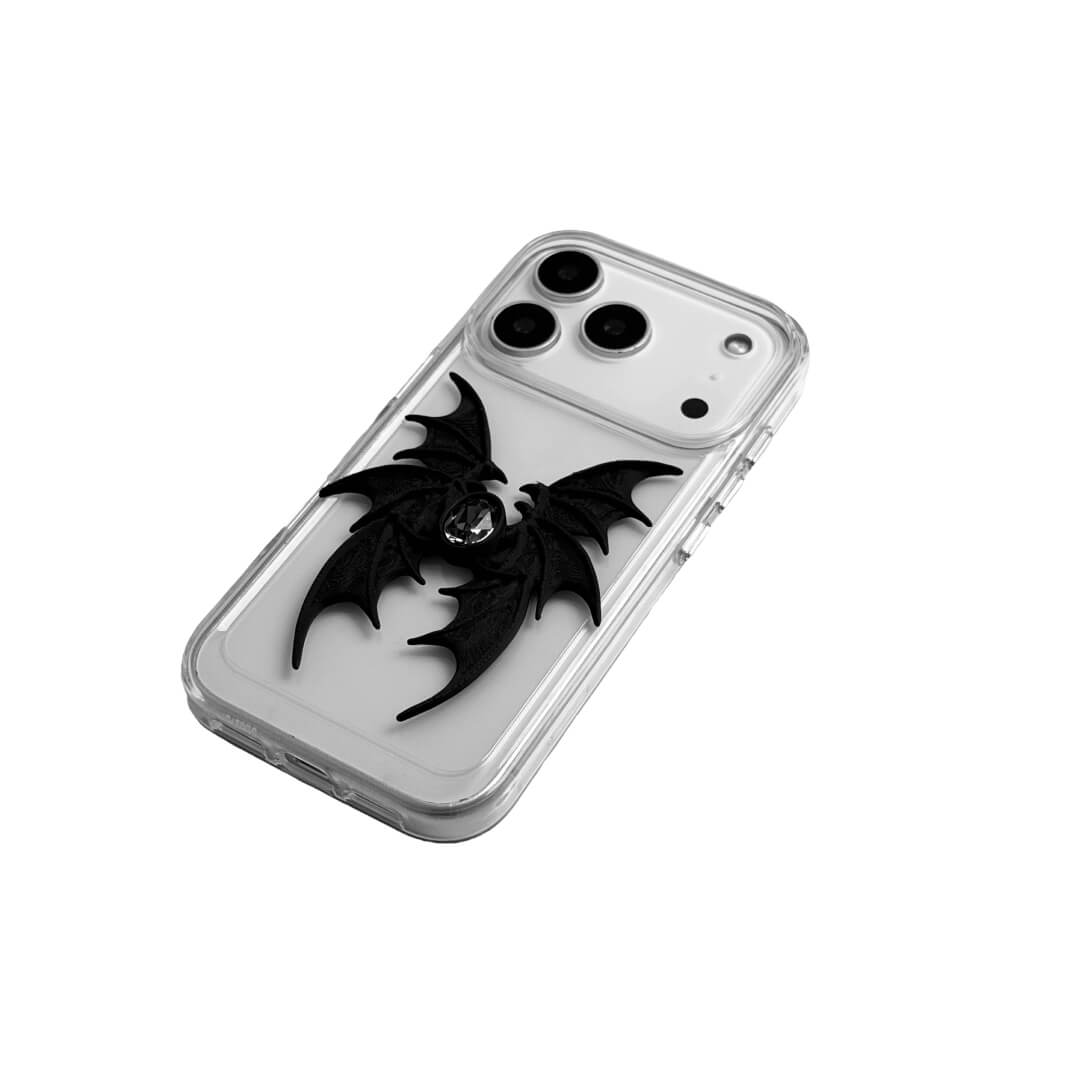 A high-concept iPhone case featuring a 3D-printed quad-wing demon design in a natural matte black finish, centered with a sparkling black Swarovski crystal. The design is shown on a Clear Transparent base and a Black Litchi Leather textured base, highlighting the intricate, layered skeletal wing structure and the dark gemstone detail.