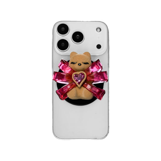 Ribbon Magic Bear Phone Grip in Pink Edition featuring a glossy pink ribbon with a beige gummy bear at the center, holding a sparkling pink heart-shaped crystal.