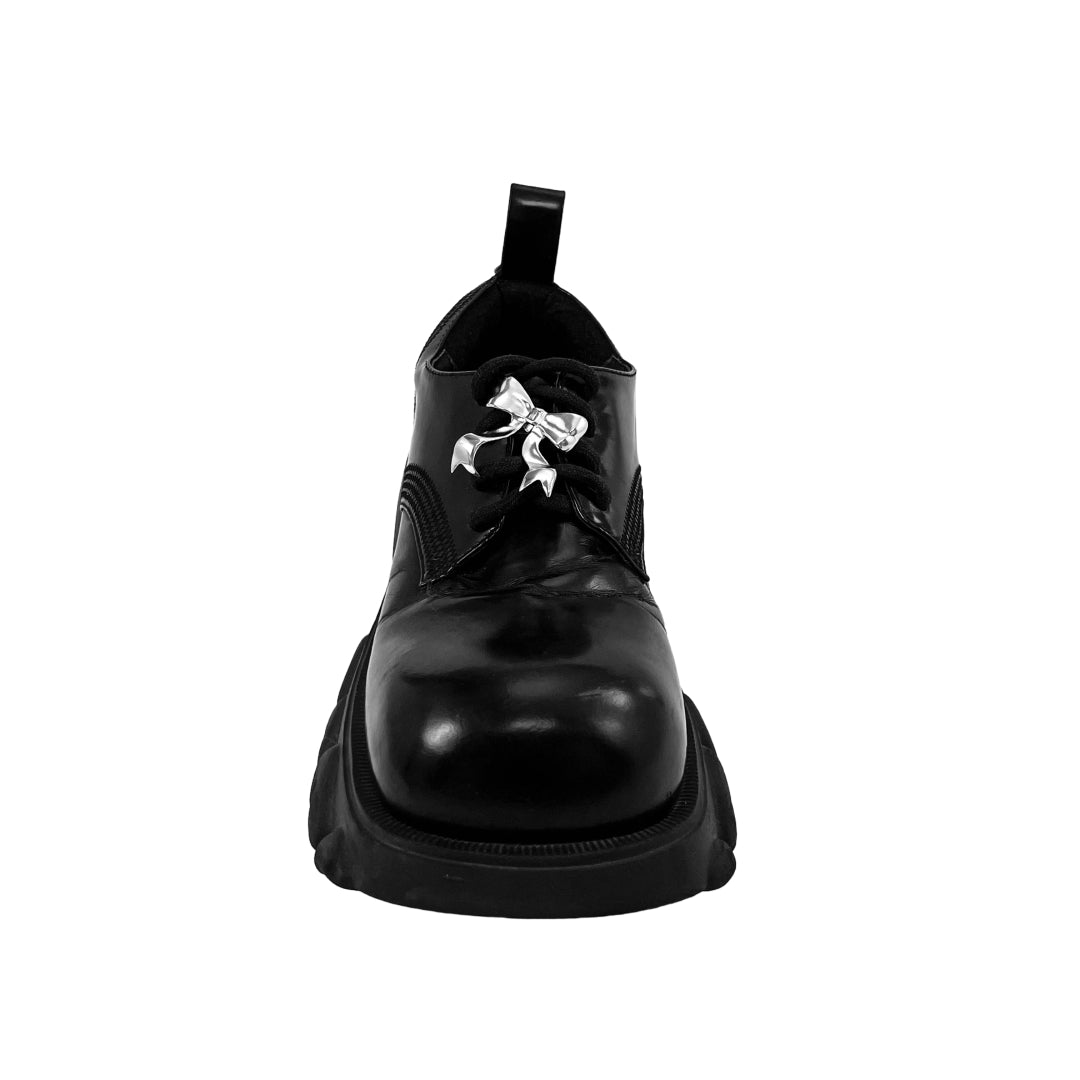 Silver bow-shaped shoe accessory clipped onto the laces of a black sneaker or boot.
