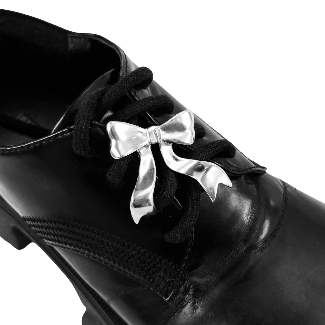 Silver bow-shaped shoe accessory clipped onto the laces of a black sneaker or boot.
