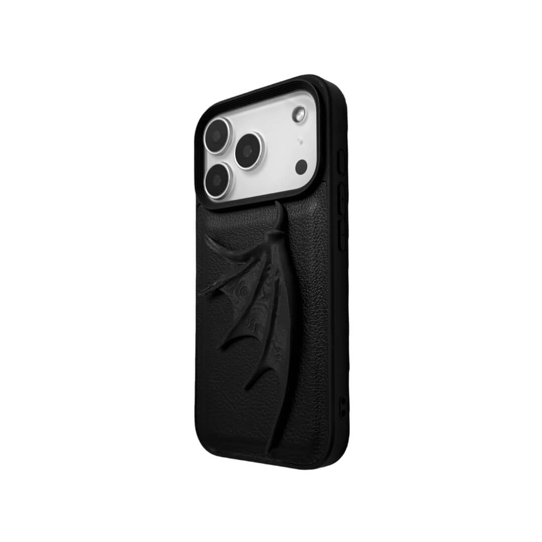 A high-fashion iPhone case featuring a large, 3D-printed single demon wing with a natural matte black finish. The design is presented in two styles: an asymmetric wing on a Clear Transparent base, and the same sculptural wing on a Black Leather textured base, showcasing a moody and avant-garde aesthetic.