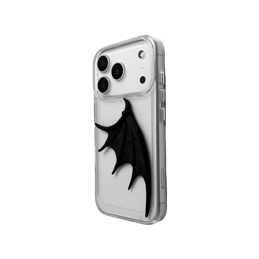 A high-fashion iPhone case featuring a large, 3D-printed single demon wing with a natural matte black finish. The design is presented in two styles: an asymmetric wing on a Clear Transparent base, and the same sculptural wing on a Black Leather textured base, showcasing a moody and avant-garde aesthetic.