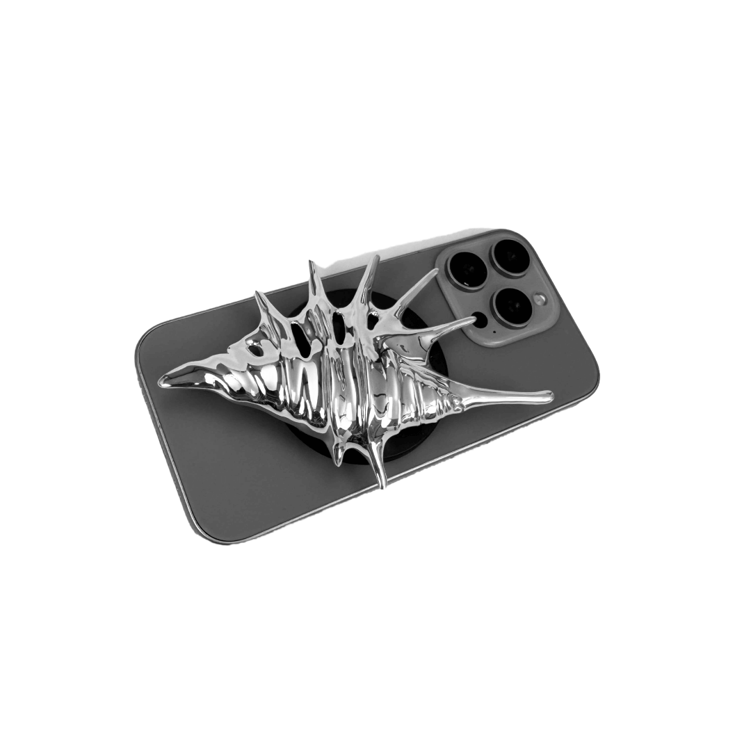Matte silver, white and yellow spiked conch shell phone grip with sculptural spikes and spiral ridges, mounted on a black base and attached to a gray iPhone case.