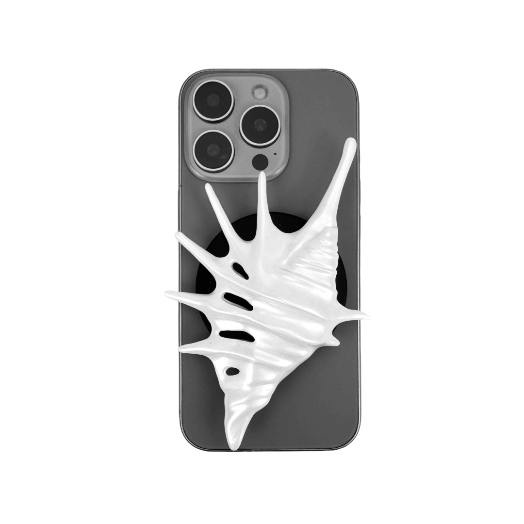Matte silver, white and yellow spiked conch shell phone grip with sculptural spikes and spiral ridges, mounted on a black base and attached to a gray iPhone case.
