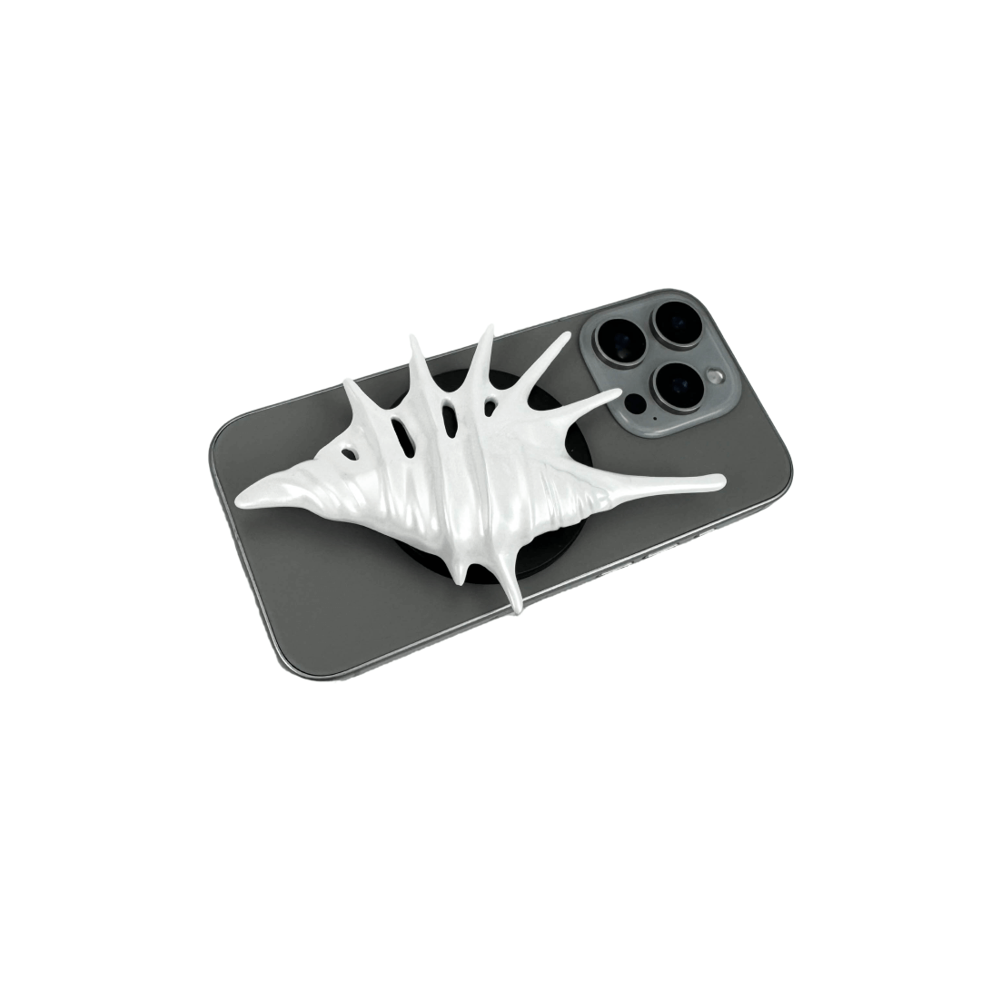 Matte silver, white and yellow spiked conch shell phone grip with sculptural spikes and spiral ridges, mounted on a black base and attached to a gray iPhone case.