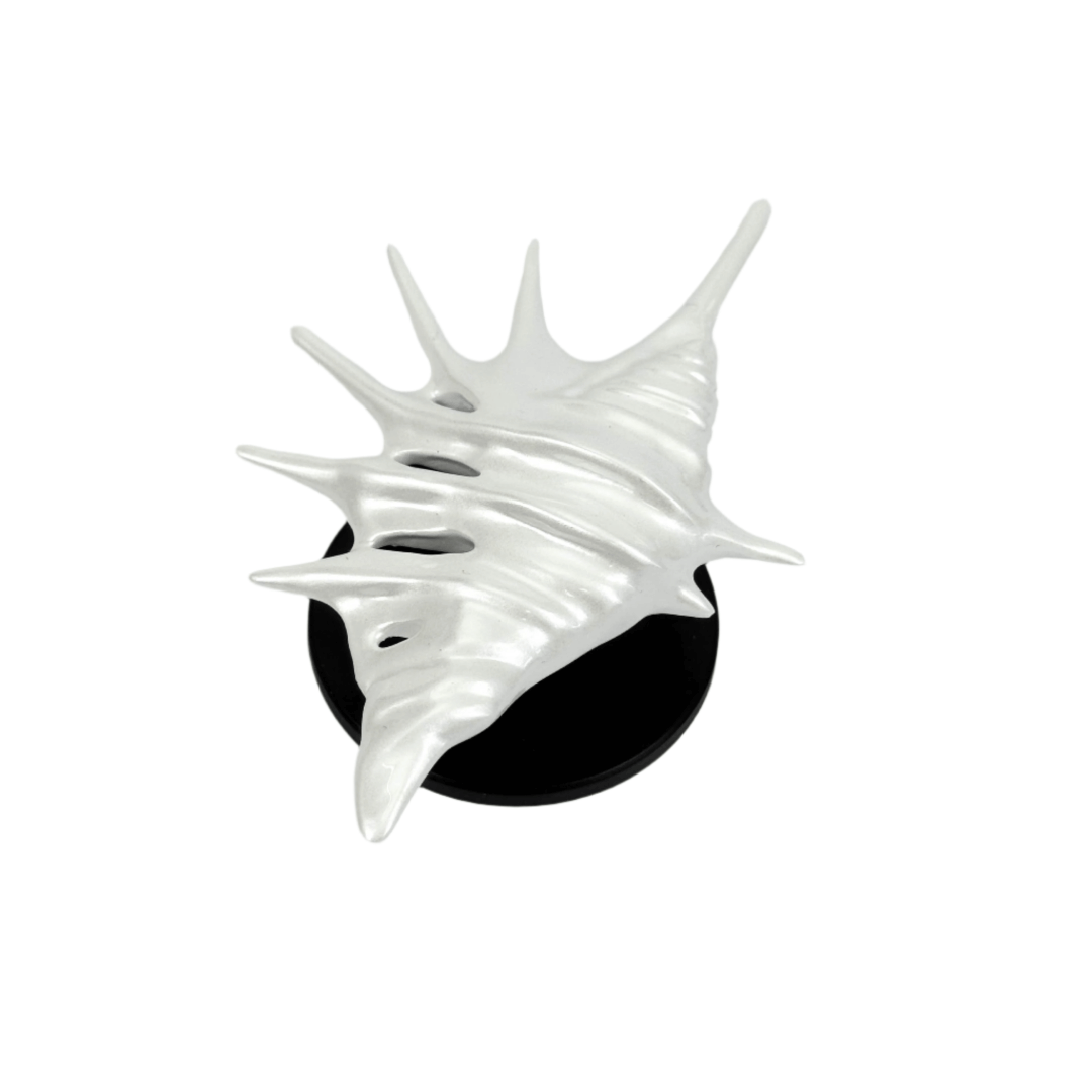 Matte silver, white and yellow spiked conch shell phone grip with sculptural spikes and spiral ridges, mounted on a black base and attached to a gray iPhone case.