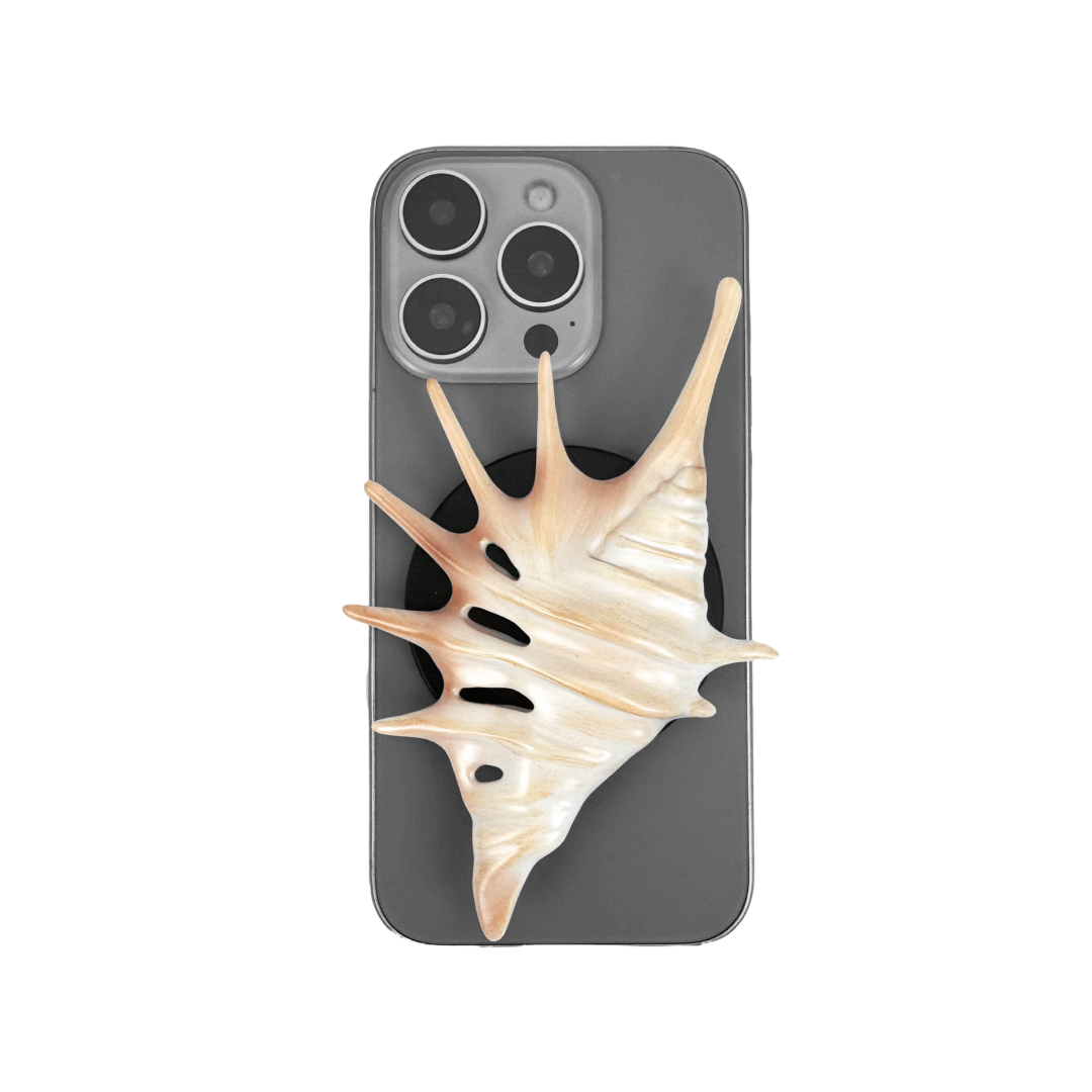 Matte silver, white and yellow spiked conch shell phone grip with sculptural spikes and spiral ridges, mounted on a black base and attached to a gray iPhone case.