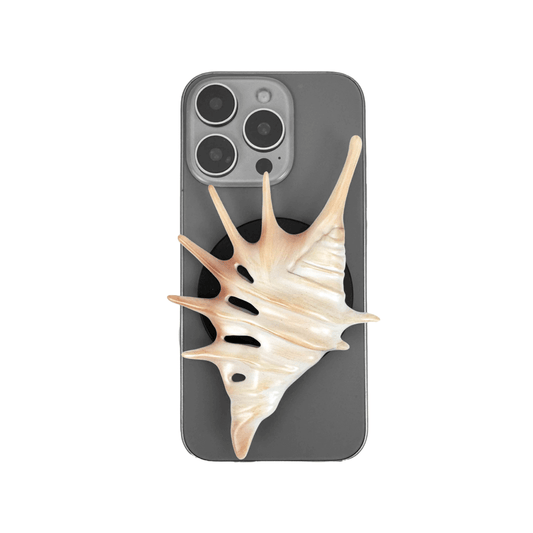 Matte silver, white and yellow spiked conch shell phone grip with sculptural spikes and spiral ridges, mounted on a black base and attached to a gray iPhone case.