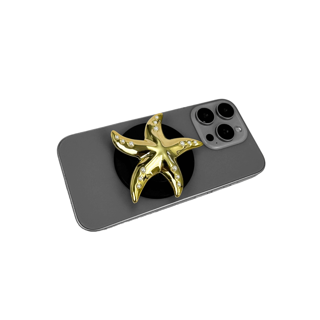 Glossy white, silver, gold and pink starfish-shaped phone grip with embedded rhinestones, mounted on a black base and attached to a gray iPhone case. 