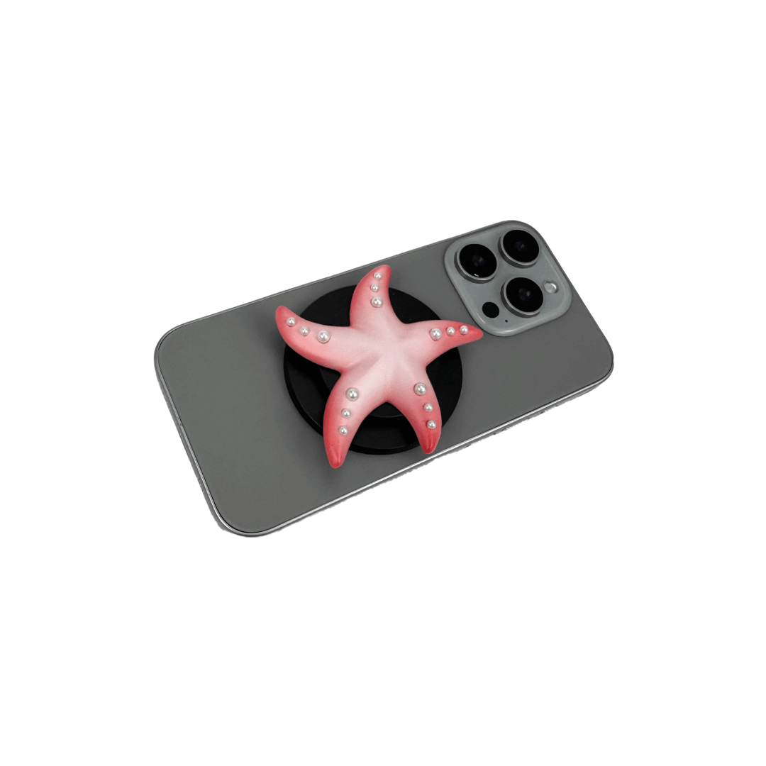 Glossy white, silver, gold and pink starfish-shaped phone grip with embedded rhinestones, mounted on a black base and attached to a gray iPhone case. 