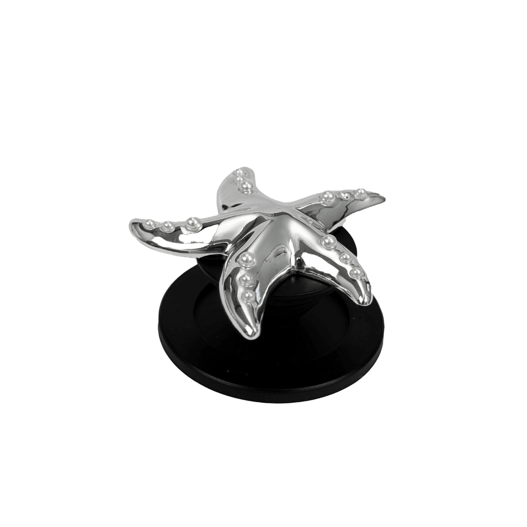 Glossy white, silver, gold and pink starfish-shaped phone grip with embedded rhinestones, mounted on a black base and attached to a gray iPhone case. 