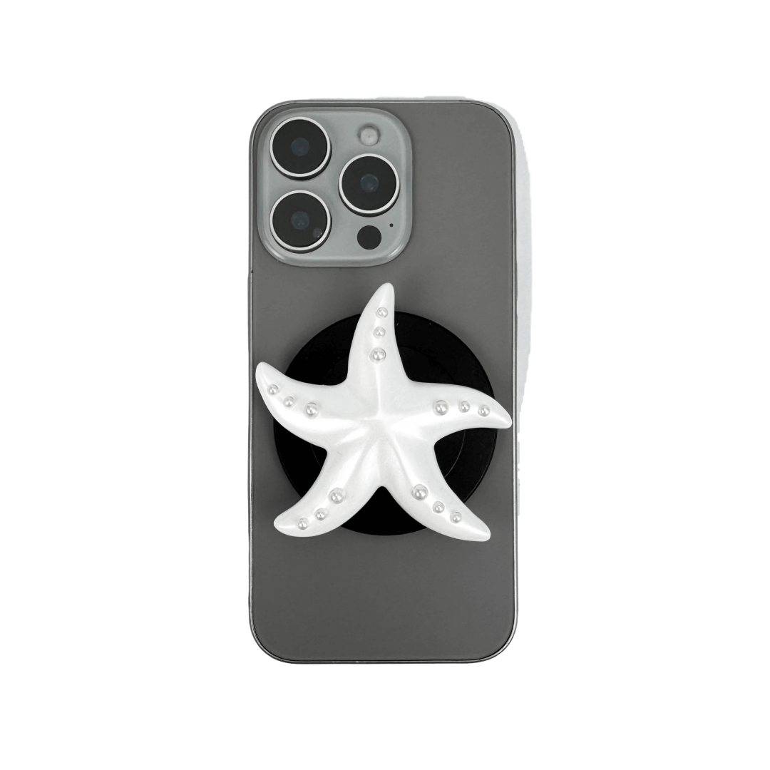 Glossy white, silver, gold and pink starfish-shaped phone grip with embedded rhinestones, mounted on a black base and attached to a gray iPhone case. 